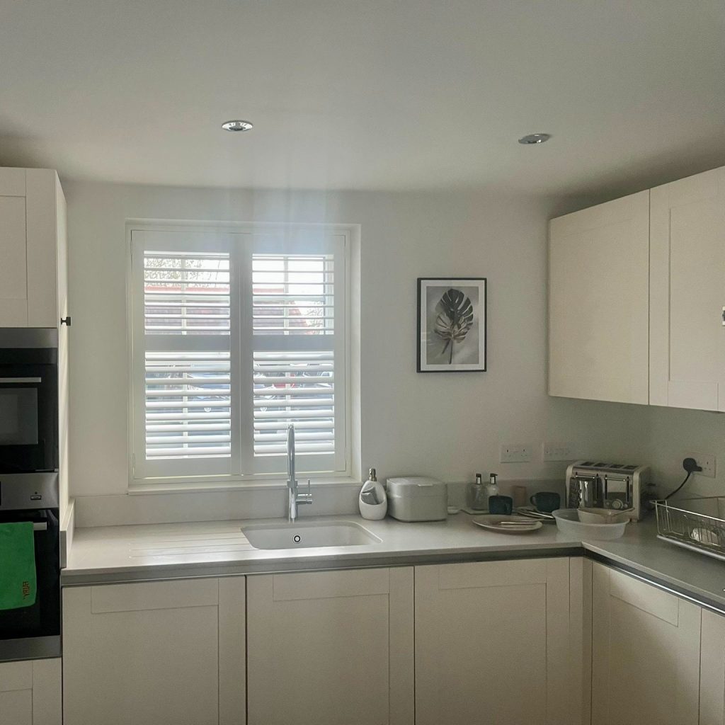 Real Shutter Envy install — white plantation shutters fitted inside a deep kitchen window recess above the sink, panels clear of the glass and opening normally.