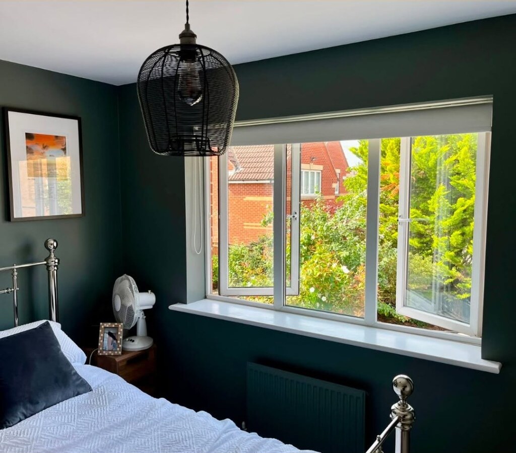 Bedroom window before shutters — white roller blind over an open casement, deep green walls
